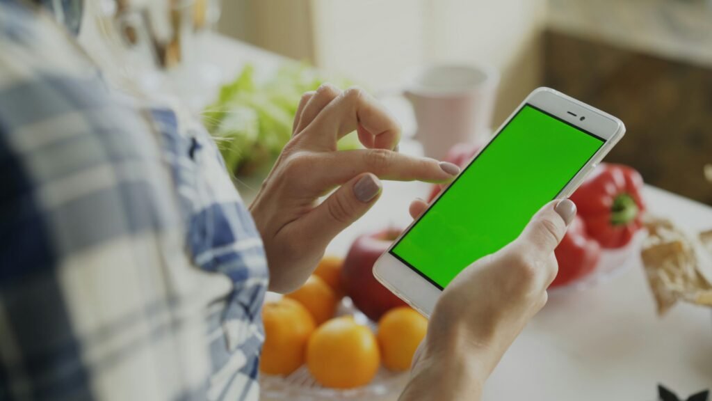 Woman scrolling her phone in the kitchen, comparing herself to other mothers online